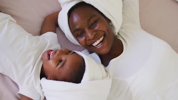 Portrait of african american mother and daughter wearing towels lying on bed and smiling