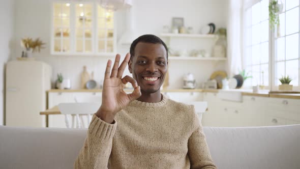 Happy African American Man Shows OK Gesture Smiling on Sofa