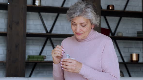 Portrait of Senior Woman Eating Yogurt Sitting on the Couch at Home