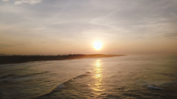 Drone Flying High Over Incredible Ocean Surface Reflecting Sunset and Waves Reaching Coast Line