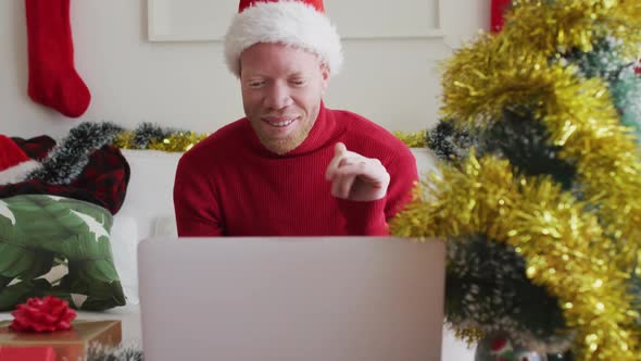 Happy albino african american man wearing santa hat making video call at christmas