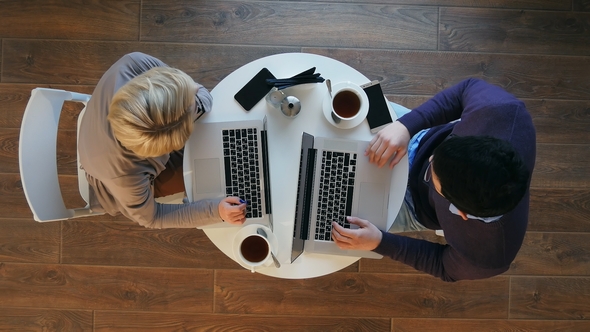 Young Successful Business Couple Is Discussing Documents, Drinking Coffee and Smiling While Working