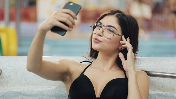Beautiful Young Woman in Black Makes Selfie on Her Smartphone in a Brand New Jacuzzi or Smimming