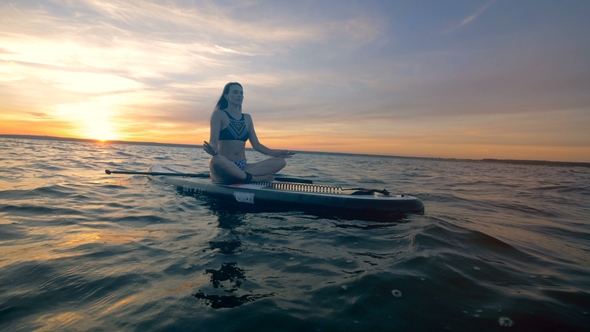 A Woman Rests on Her Paddleboard in the Ocean, Meditating