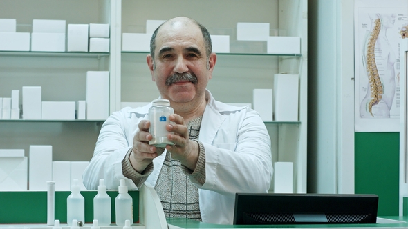 Smiling Doctor Holding Up a Bottle of Tablets Advacing It To a Customers Looking To a Camera