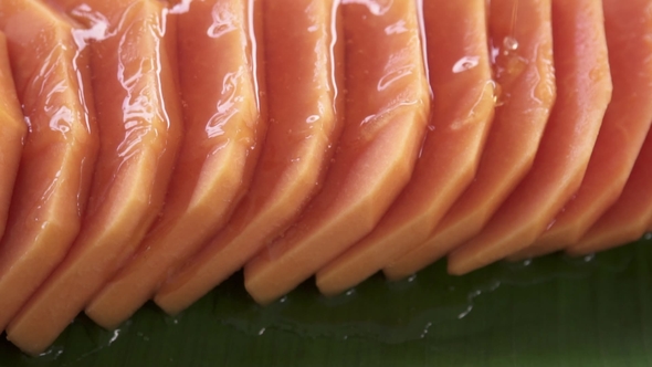 Pouring Syrup Onto Slices of Fresh Raw Exotic Tropical Thai Fruit Carica Papaya Rotating on Banana