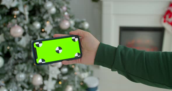 Man Hand Holding the Black Smartphone with Green Screen on Christmas Decorated Background