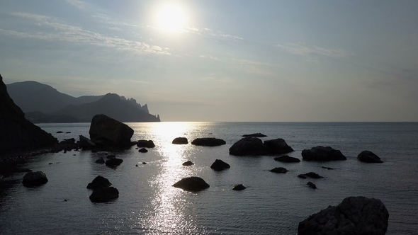 Flying Backward Over the Sea Surface with Rocks and Stones at Sunrise. Mountains, Rocks, Stones in