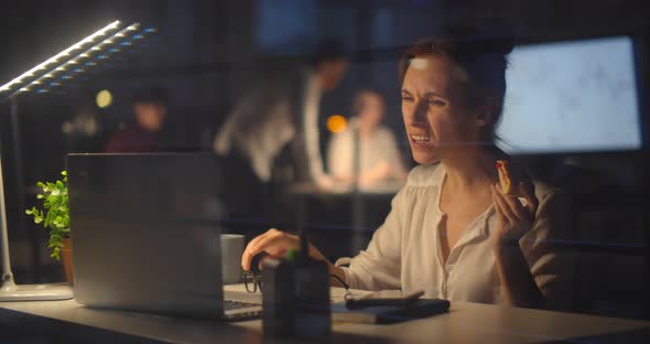 Businesswoman Eating Pie at Desk Working in Office Late in Evening