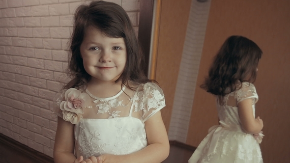 A Beautiful Little Girl with Painted Lips Looks in the Mirror.