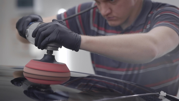 Master Is Grinding a Roof of Clean Black Automobile During Making Protective Covering in a Garage