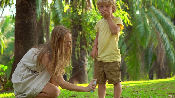 Young Woman in a Tropical Park Puts a Mosquito Repellent on Her Son