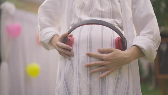 Closeup Headphones on Pregnant Belly of Unrecognizable Caucasian Woman Dancing in Slow Motion