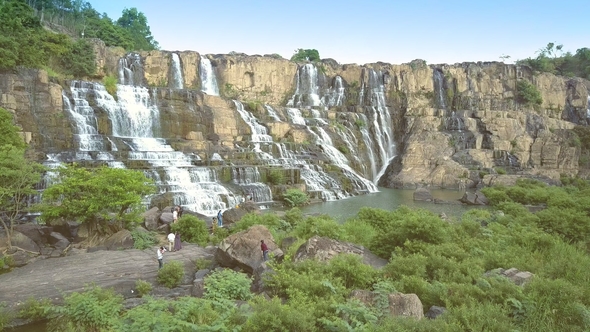 Tourists Stand on Rocks Enjoy Waterfall Cliffs at Sunset