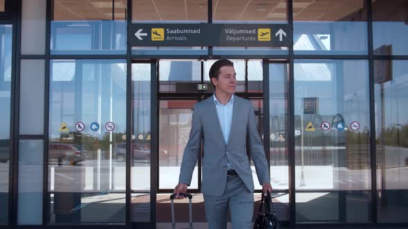 Elegant businessman walking with suitcase along the airport. Young mail entrepreneur.