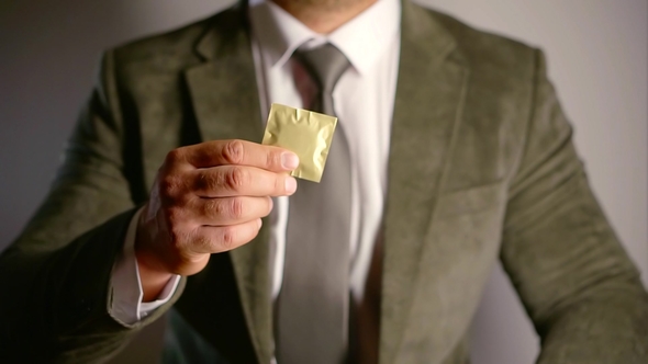 Agent Holding a Single Condom in a Golden Package and Putting It in Inner Pocket of a Jacket