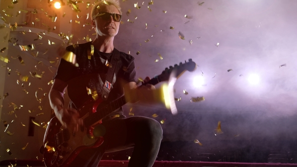 The Guitarist Performs on Stage. Stage Light, Smoke. From Above Fall Golden Confetti