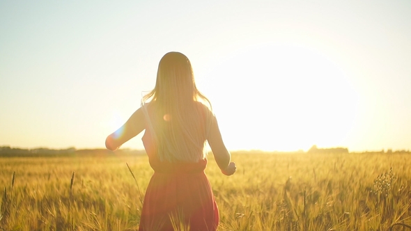 A Girl in a Red Dress Runs Across the Field at Sunset