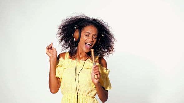 Young Cute African American Woman in Yellow Dress Singing and Dancing with Hair Dryer