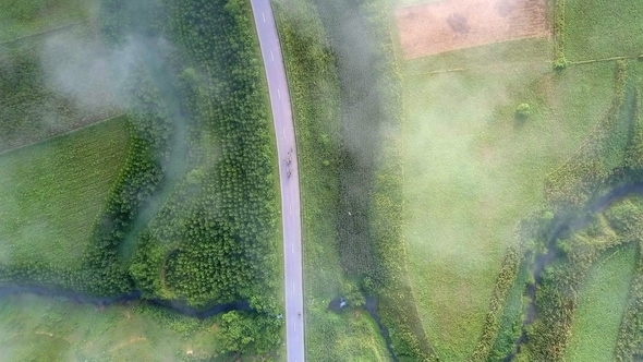 Flycam Descends To Road with Traffic Among Green Landscape