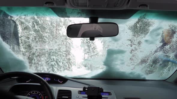 Couple Cleaning Snow From Car Windshield