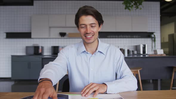 Smiling caucasian businessman having video chat going through paperwork in workplce kitchen