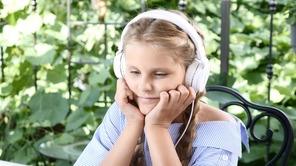 Portrait of Pretty Girl Sitting in a Street Cafe with Notebook on Table and Earphones on Her Head