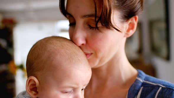 Young mom holding and kissing her baby at home 4k