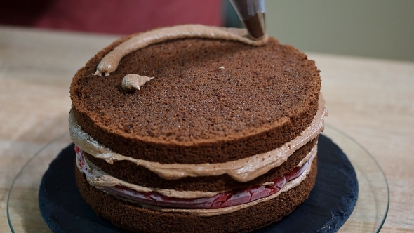 Unrecognizable Female Pastry Cook Squeezing Chocolate Cream on Appetizing Layer Cake in Kitchen