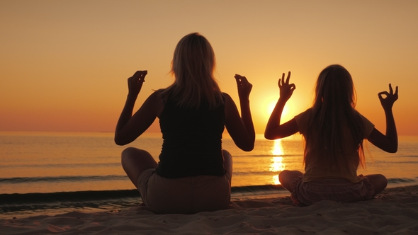 Mom and Daughter Are Meditating By the Sea at Sunset