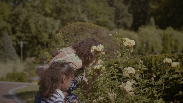 Joyful Mother with Kids Smelling Flowers in Garden