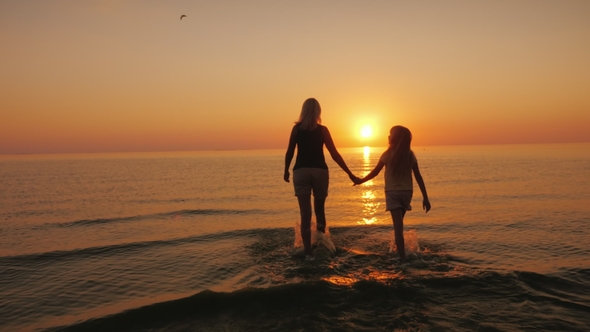 Mom and Daughter Are Walking on the Water Against the Backdrop of the Setting Sun