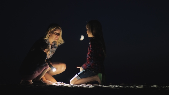 Mom with Two Daughters Playing in the Sand on the Beach in the Late Evening