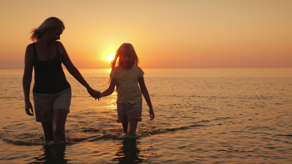 A Young Mother with a Child Is Walking on the Water in Shallow Water