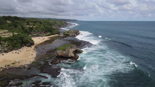 Aerial view of tropical beach in Gunung kidul, Indonesia with green and rocky cliff.