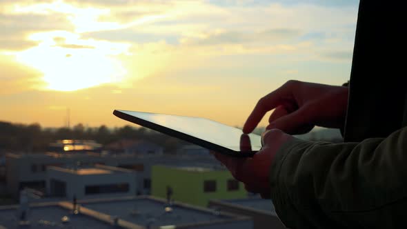 Man Works on a Tablet, Sunset in the Background - Closeup of Hands