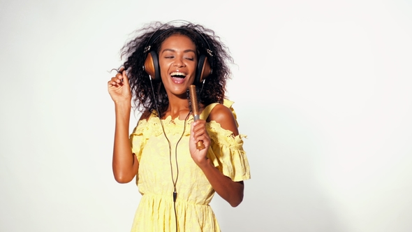 Young Pretty African American Woman in Yellow Dress Singing and Dancing with Hair Dryer Instead