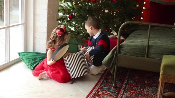 Happy Children Sister and Brother Open Gifts Sitting on the Floor Under Christmas Tree