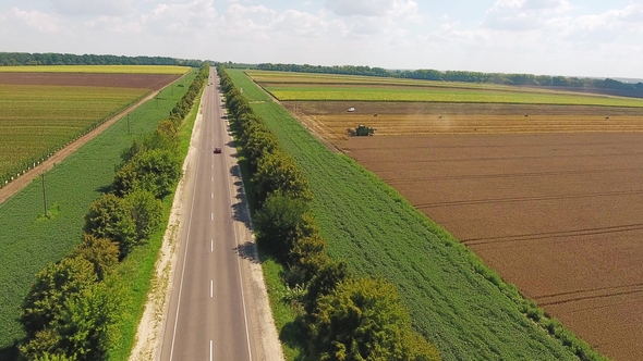 Highway with Cars Near Agricultural Fields Where There Is Harvesting