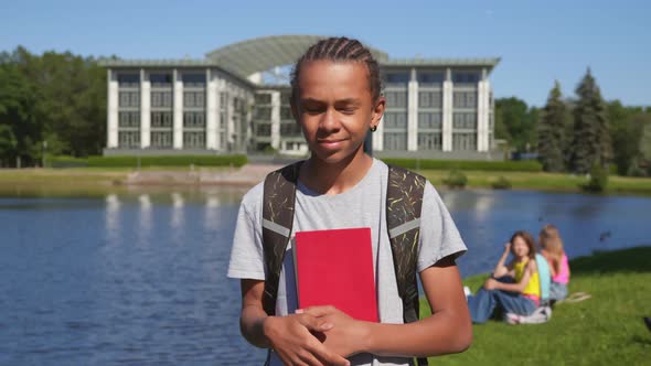 Medium Shot of African Student Boy Holding Book and Looking at Camera at Park