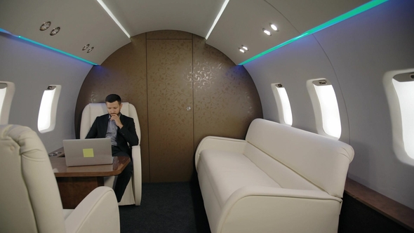 Young Confident Lawyer Businessman Is Working with Laptop Sitting in Entrepreneur Airplane Interior