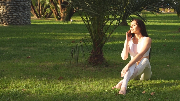 Yoga Girl Sitting on Grass, Talking on Smartphone in Park