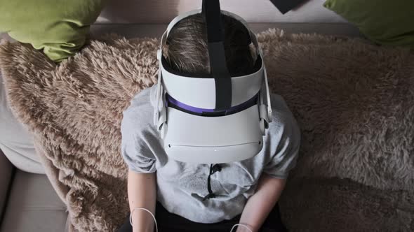 Young Woman in Virtual Reality Helmet Sitting on Sofa and Move Hands at Home