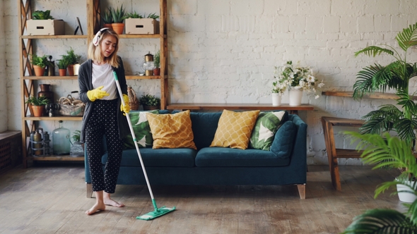 Attractive Girl in Headphones Is Listening To Music and Dancing Wih Mop During Domestic Work