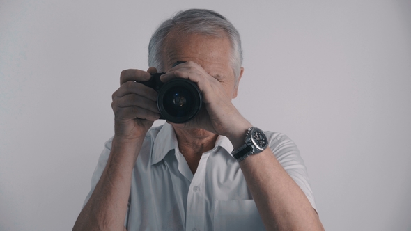 Gray Haired Senior Man Photographer Takes Shots with His Photo Camera at White Background