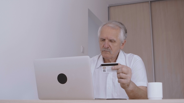 Senior Man Online Shoping at Home on Laptop, Typing Credit Card Number