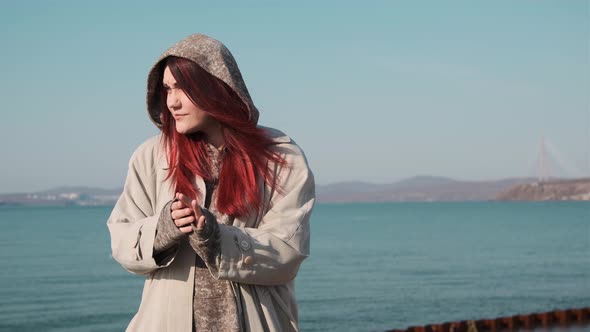 one girl in a coat stands on the shore of a calm sea