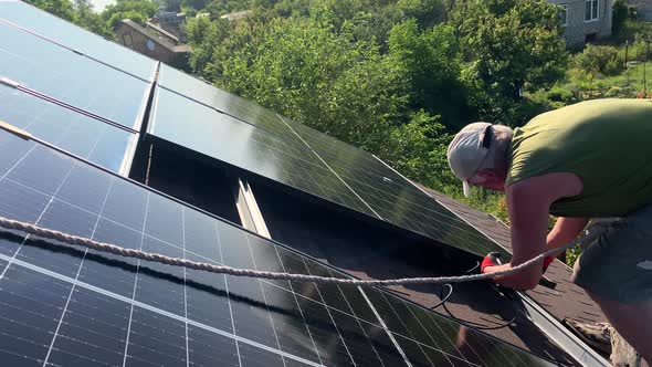 Worker Fasten Bolt Installs Solar PV Panels on Bituminous Tiles Roof of Small House