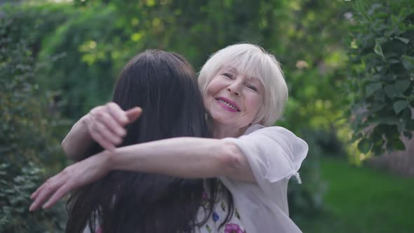 Happy Senior Elegant Woman Hugging Young Granddaughter in Slow Motion Smiling Looking at Camera