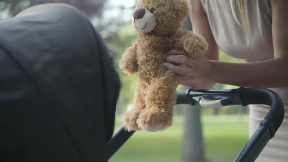 Unrecognizable Slim Caucasian Mother Playing Teddy Bear in Front of Baby Stroller. Happy Young Woman